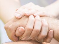 Eine junge und eine ältere Person umschließen einander die Hände.  - Öffnet große Ansicht