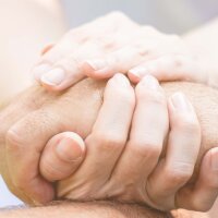 Eine junge und eine ältere Person umschließen einander die Hände.  - Öffnet große Ansicht